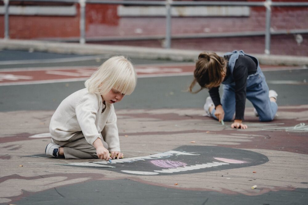 little girls on asphalt with chalks drawing